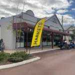 A storefront with a large yellow sign that reads “MARKETS,” with motorcycles parked in front and a person walking toward the entrance.